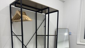 A room with a black metal shelving unit with three shelves, a wooden floor, and a bed with a white and black patterned bedspread.