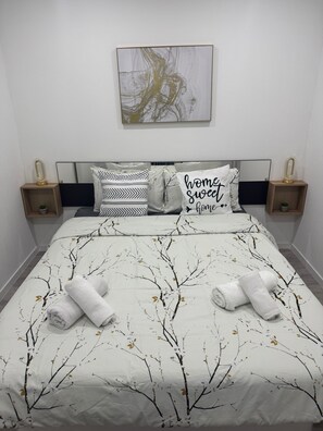 A neatly made bed with a tree branch pattern bedspread, two pillows with black and white patterns, and a wall-mounted abstract art piece.