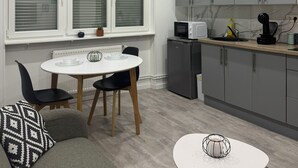 A modern kitchen with grey cabinets, a white dining table, and a grey sofa with patterned cushions.