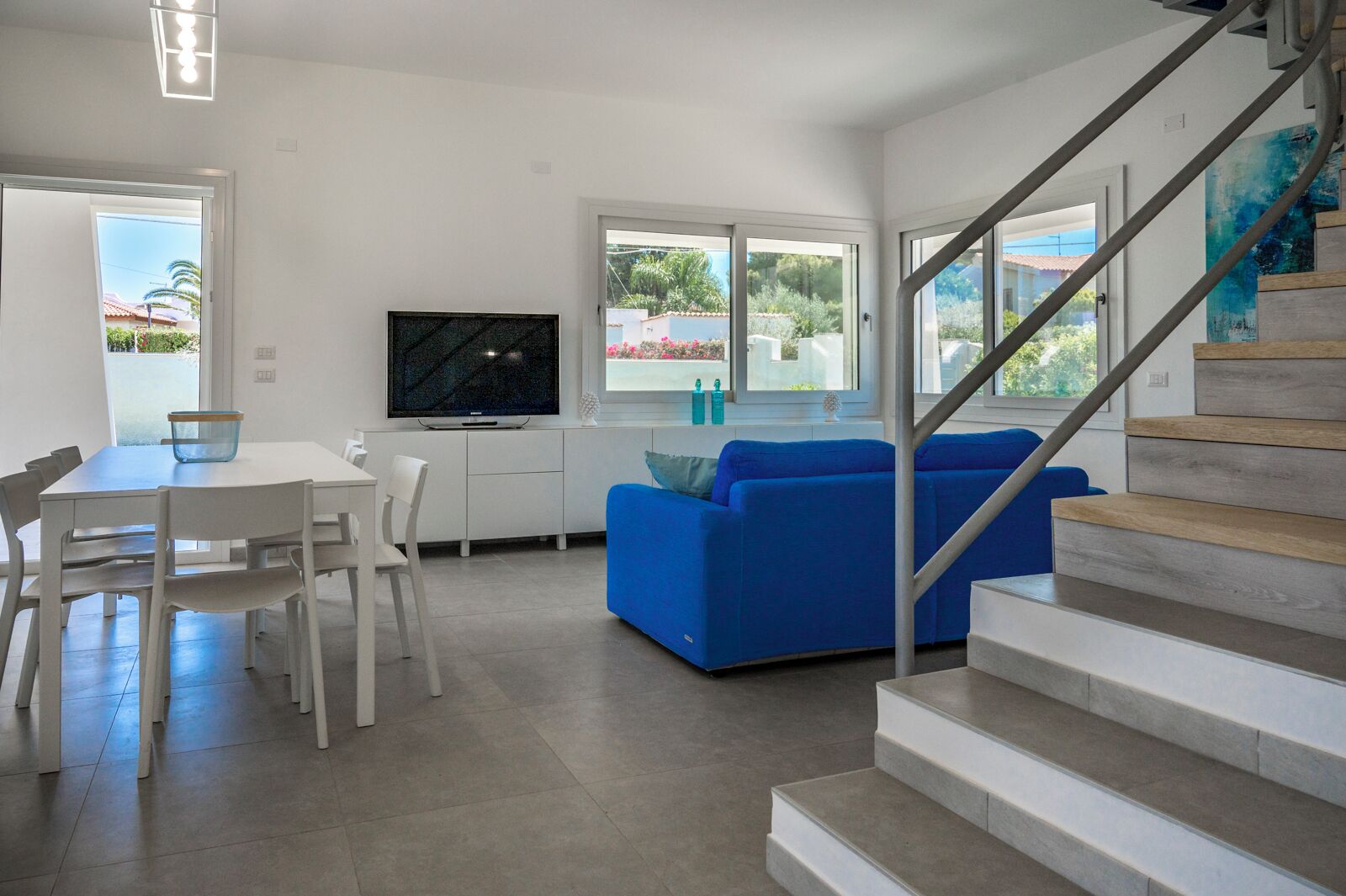 Un salon moderne avec un coin repas, un escalier et de grandes fenêtres.