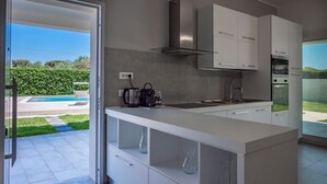 Een moderne keuken met witte kastjes, een inbouwoven en uitzicht op een zwembad.