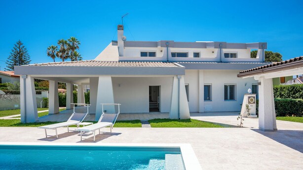 Een modern huis met zwembad, overdekt terras en een verzorgd gazon.