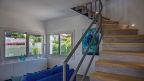 Een moderne woonkamer met een blauwe bank, een houten trap en grote ramen met uitzicht op de tuin.
