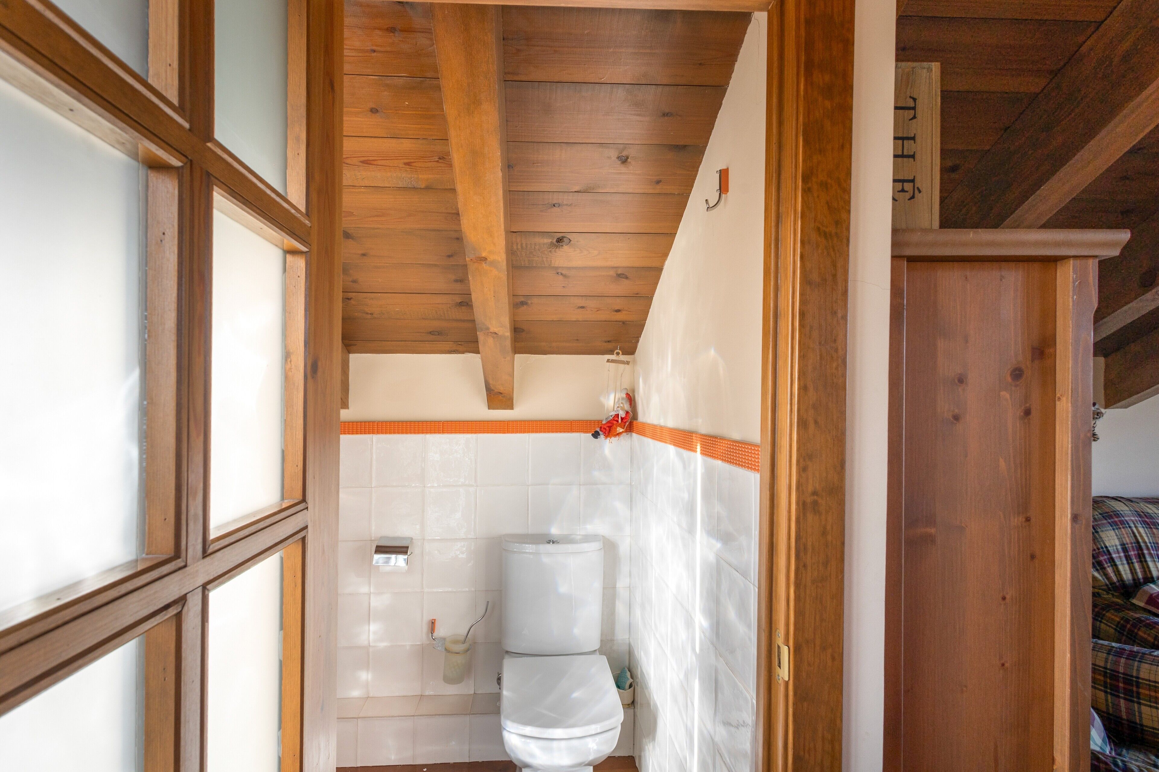 A wooden ceiling, a white toilet, and a tiled wall.