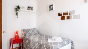 A neatly arranged bedroom with a bed, a red nightstand, a wall-mounted shelf with decorative items, and a geometric wall art piece. - Homiday - Jasmine One Min[Hospital][Airport-Free Parking] (Pisa)