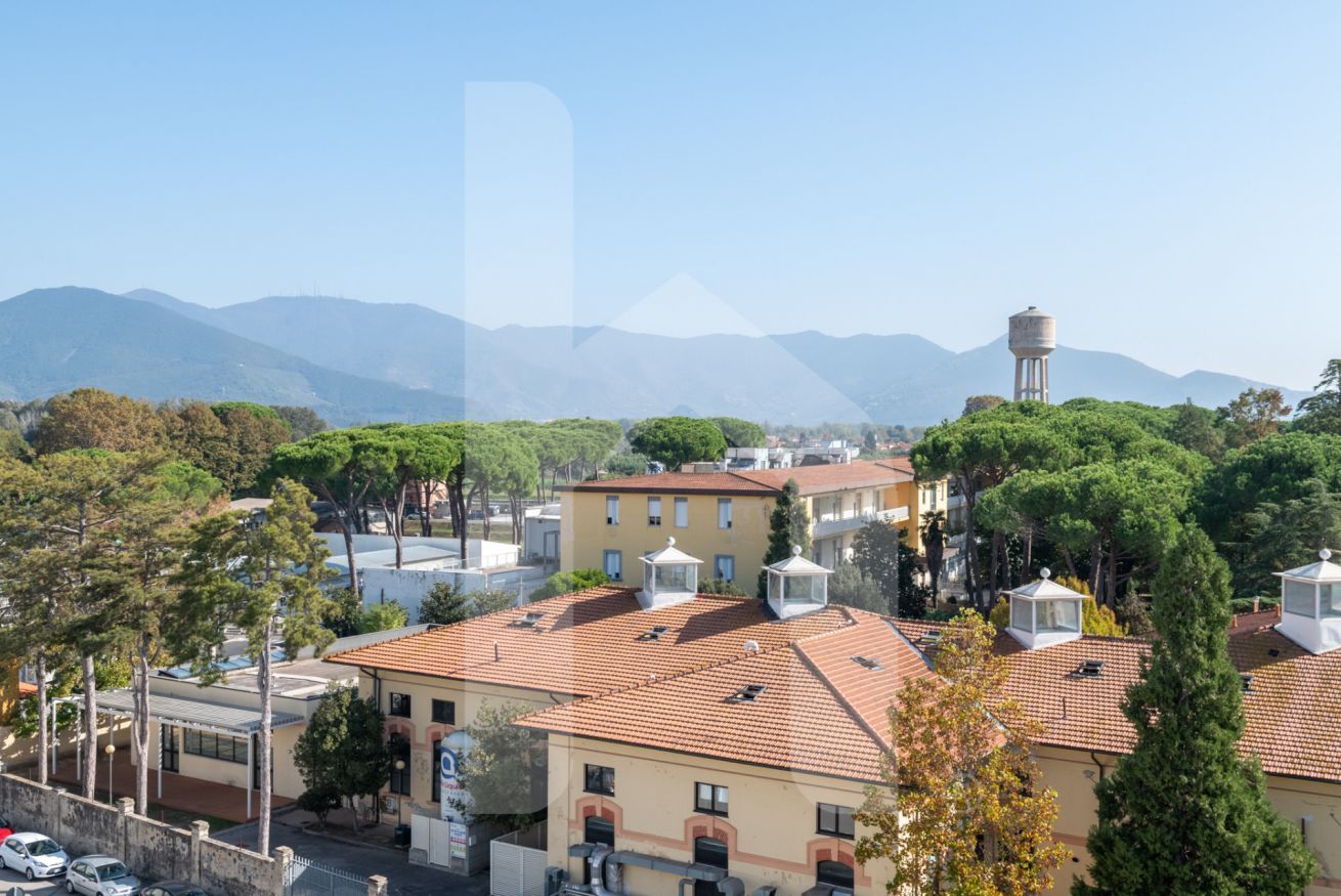 A residential area with terracotta-tiled roofs, a water tower, and a clear view of distant mountains.