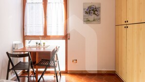 A dining area with a wooden table and chairs, a window with curtains, a wall-mounted picture, and a wooden wardrobe. - Homiday - Jasmine One Min[Hospital][Airport-Free Parking] (Pisa)