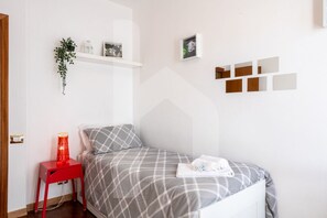 A neatly arranged bedroom with a bed, a red nightstand, a wall-mounted shelf with decorative items, and a geometric wall art piece. - Homiday - Jasmine, 1 min away [Hospital][Airport—Free Parking] (Pisa)