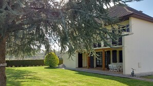 A two-story house with a covered patio, a lawn, and a small tree.