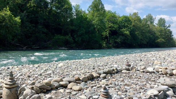 A riverbank with a pebble-strewn path and a stack of stones.