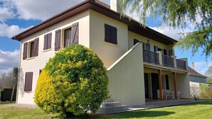 A two-story house with a balcony, a well-maintained lawn, and a large bush in the foreground.