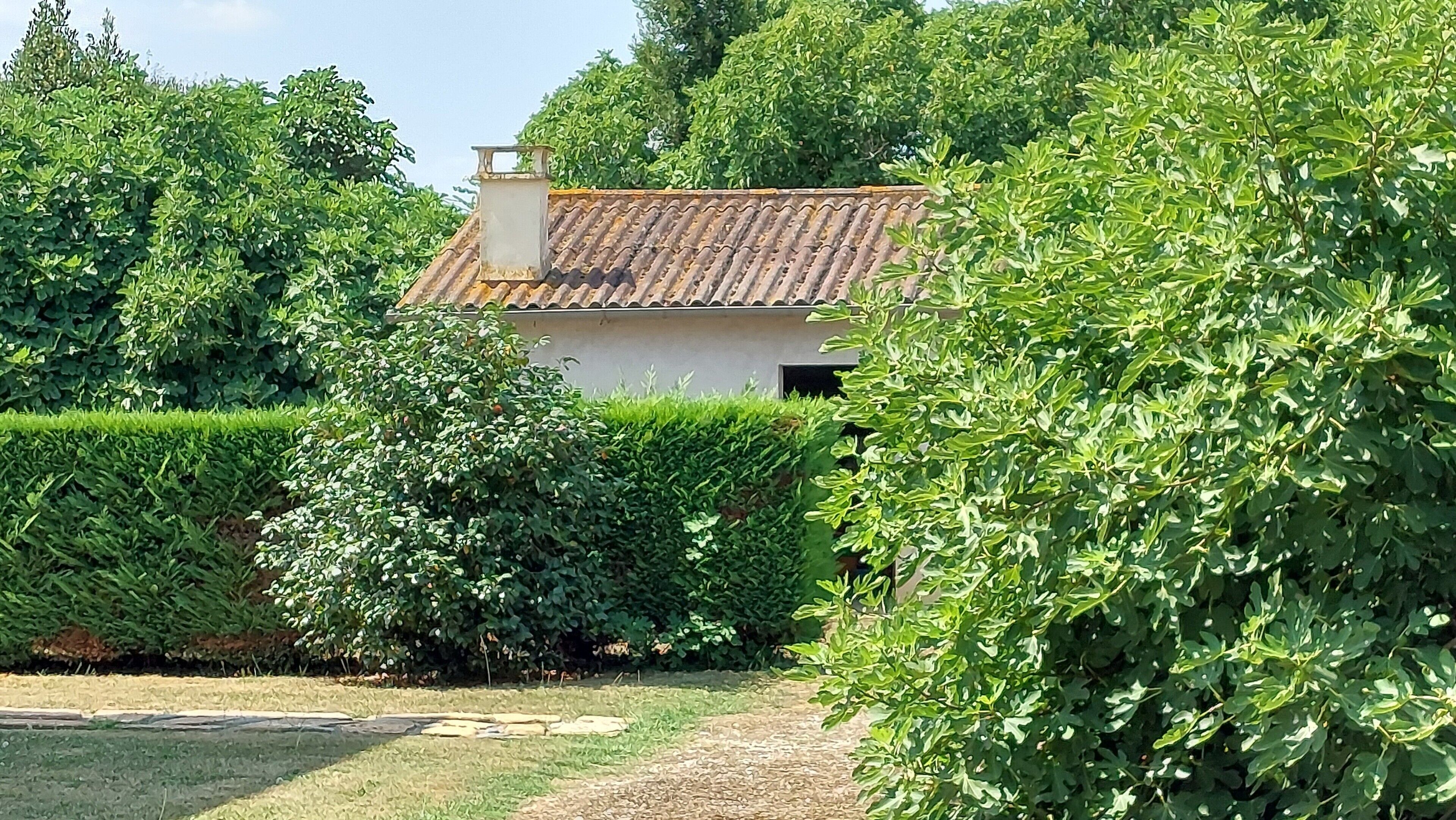 Una casa con tetto in tegole, circondata da siepi curate e alberi.