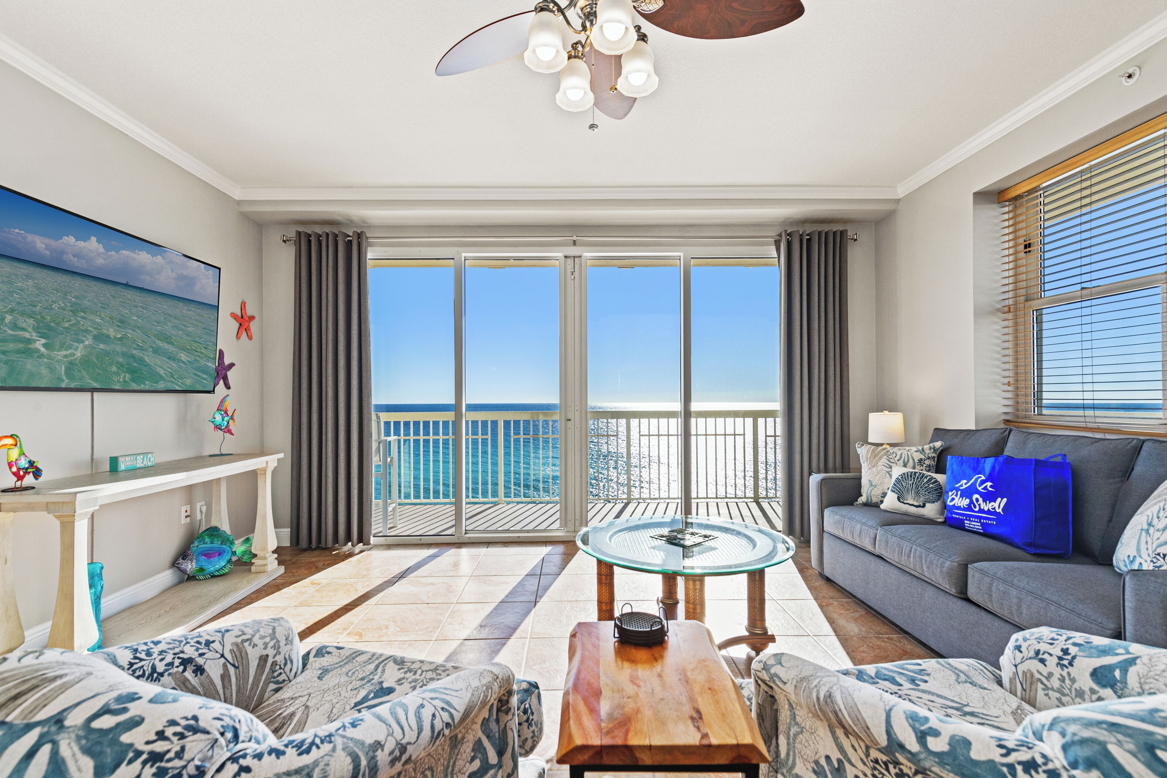 Un salon spacieux avec un balcon donnant sur la mer, un téléviseur à écran plat et une table basse en bois.