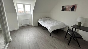 Ein kleines Zimmer mit einem Einzelbett, einer geneigten Decke, einem Fenster mit Ausblick, einem Schreibtisch mit Stuhl und einer Heizung.