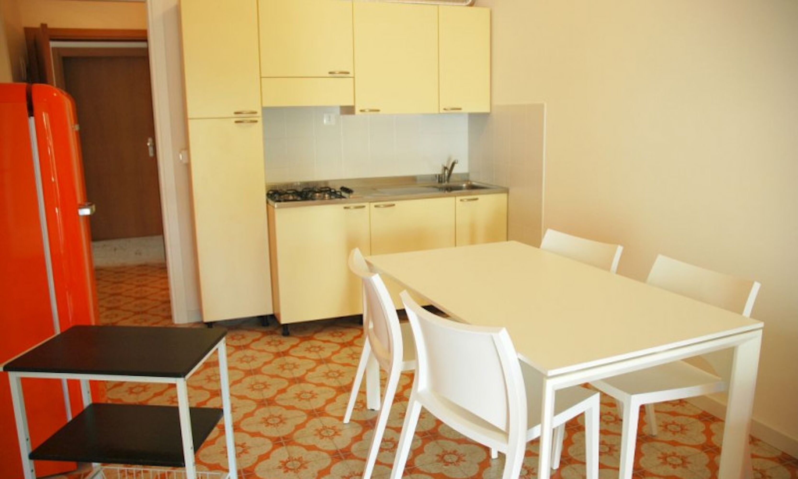 A compact kitchen with a dining area, featuring a small table and chairs, a refrigerator, and basic cabinetry.