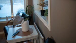 A cozy room with a view of a snowy landscape through a large window. There is a small table with a remote control and a potted plant. - Cosy and charming  2-bedroom apartment in delightful Fauske for 1-6 persons (Fauske)