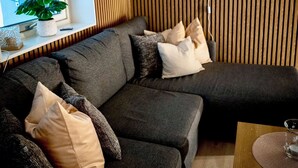 A modern living room with a sectional sofa, a round mirror, a wooden slat wall, and a window with blinds. - Cosy and charming  2-bedroom apartment in delightful Fauske for 1-6 persons (Fauske)