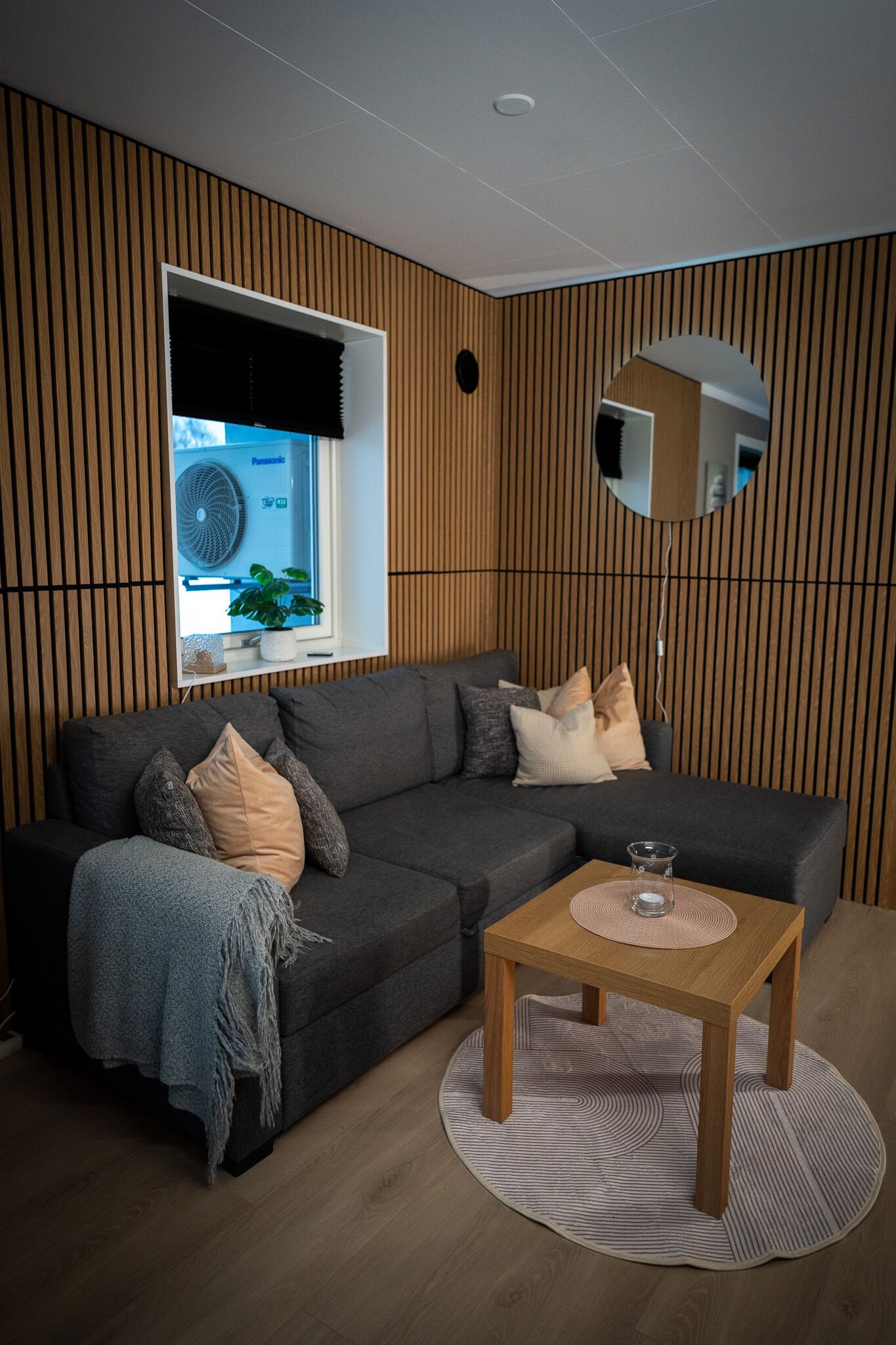 A modern living room with a sectional sofa, a round mirror, and a small wooden table.