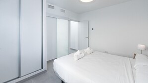 A modern hotel room with a large bed, a bedside table, a lamp, and a wardrobe.