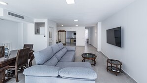 A modern living room with a sectional sofa, a dining table with chairs, a coffee table, and a TV mounted on the wall.