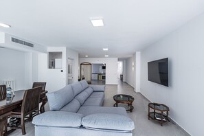 Ein modernes Wohnzimmer mit einem Ecksofa, einem Esstisch mit Stühlen, einem Couchtisch und einem an der Wand befestigten Fernseher.
