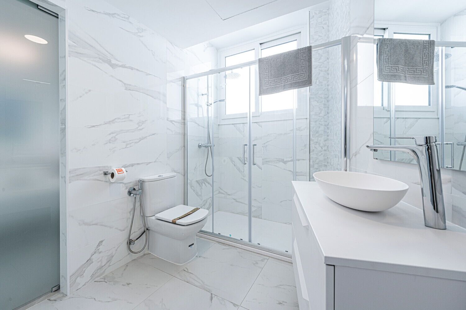 Un baño moderno con ducha de vidrio, inodoro blanco y un lavabo grande blanco con lavamanos tipo cuenco.