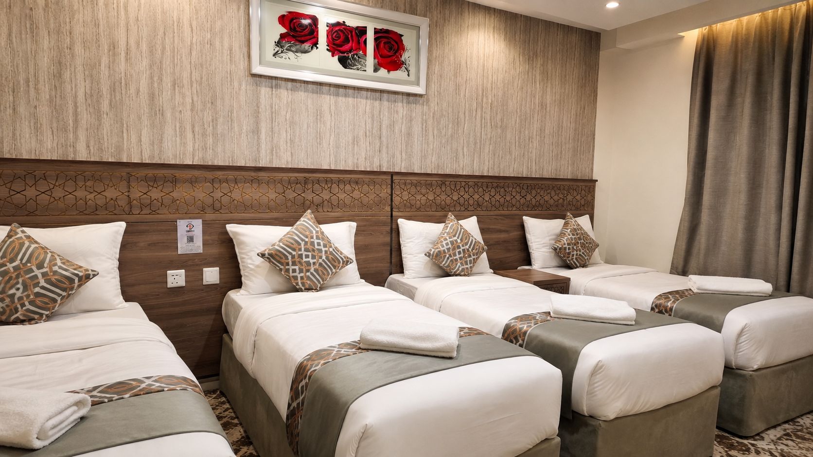 A hotel room with multiple beds, a decorative headboard, and a framed artwork above the beds.