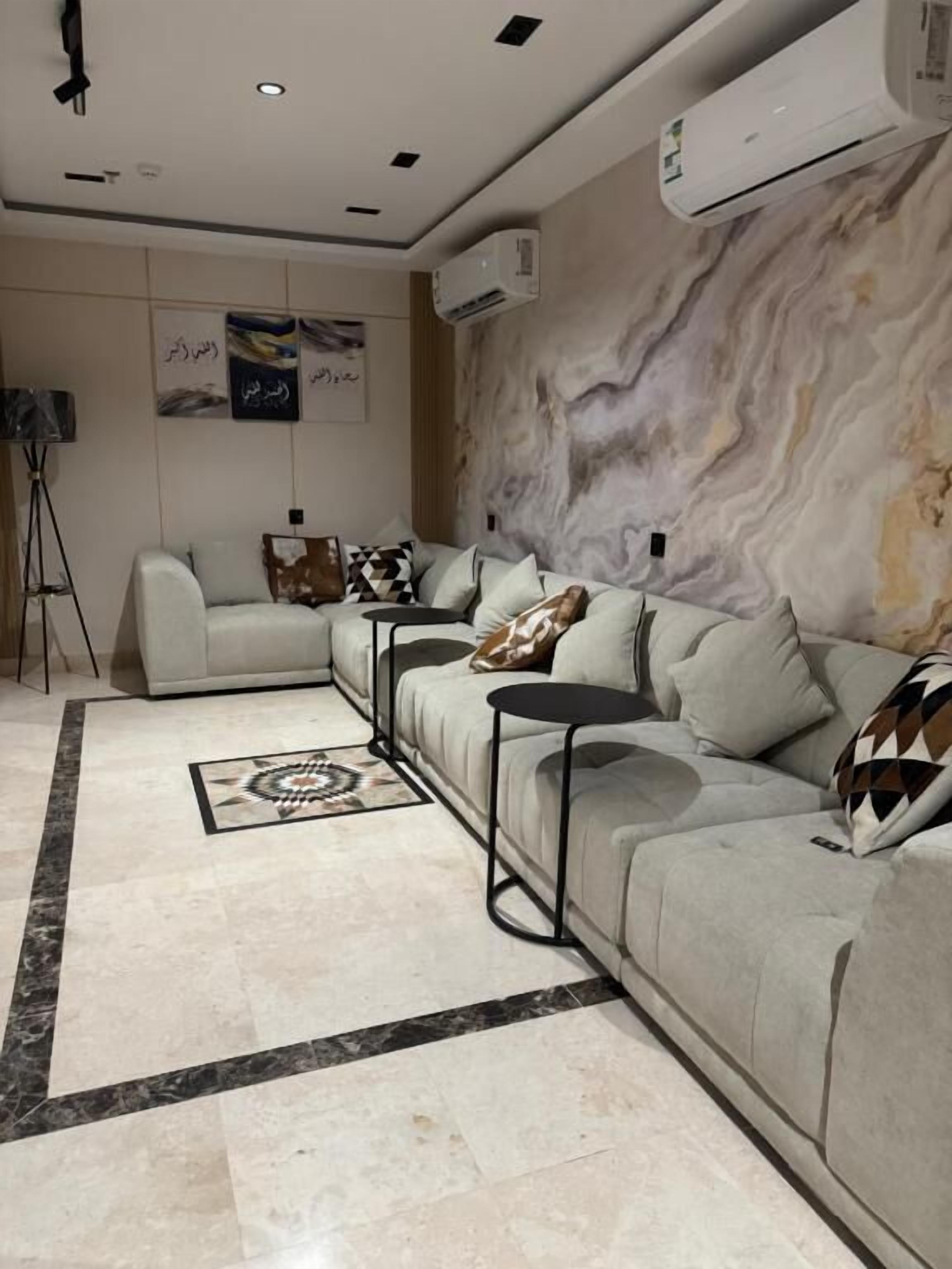 A modern living room with a beige sofa, a patterned rug, and a marble wall.