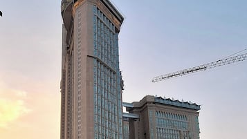 Un edificio de gran altura con una destacada torre de reloj, una amplia entrada de arco y una calle concurrida debajo.
