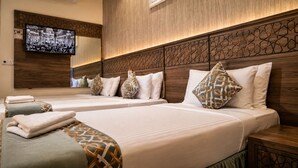 A hotel room with two beds, a television mounted on the wall, and a wooden headboard with a geometric pattern. - Zahret Alforsan Hotel (Makkah)