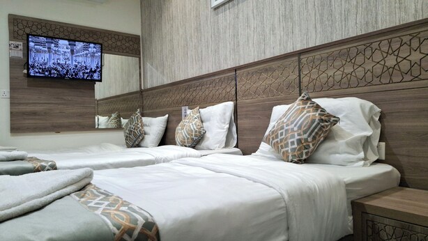 Une chambre d’hôtel avec deux lits, un téléviseur fixé au mur et une tête de lit en bois.