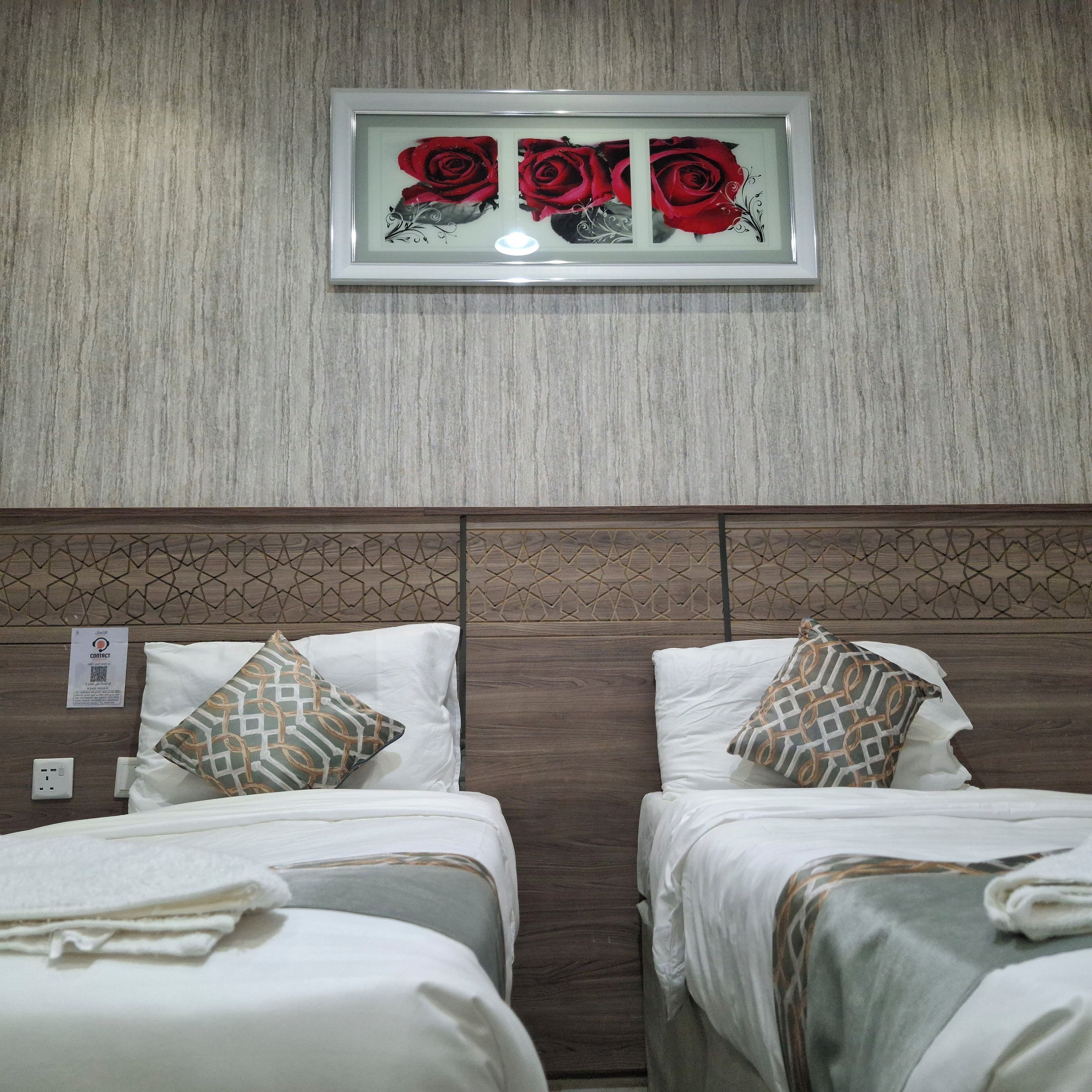 A hotel room with two beds, each with patterned pillows and a framed artwork of red roses above.