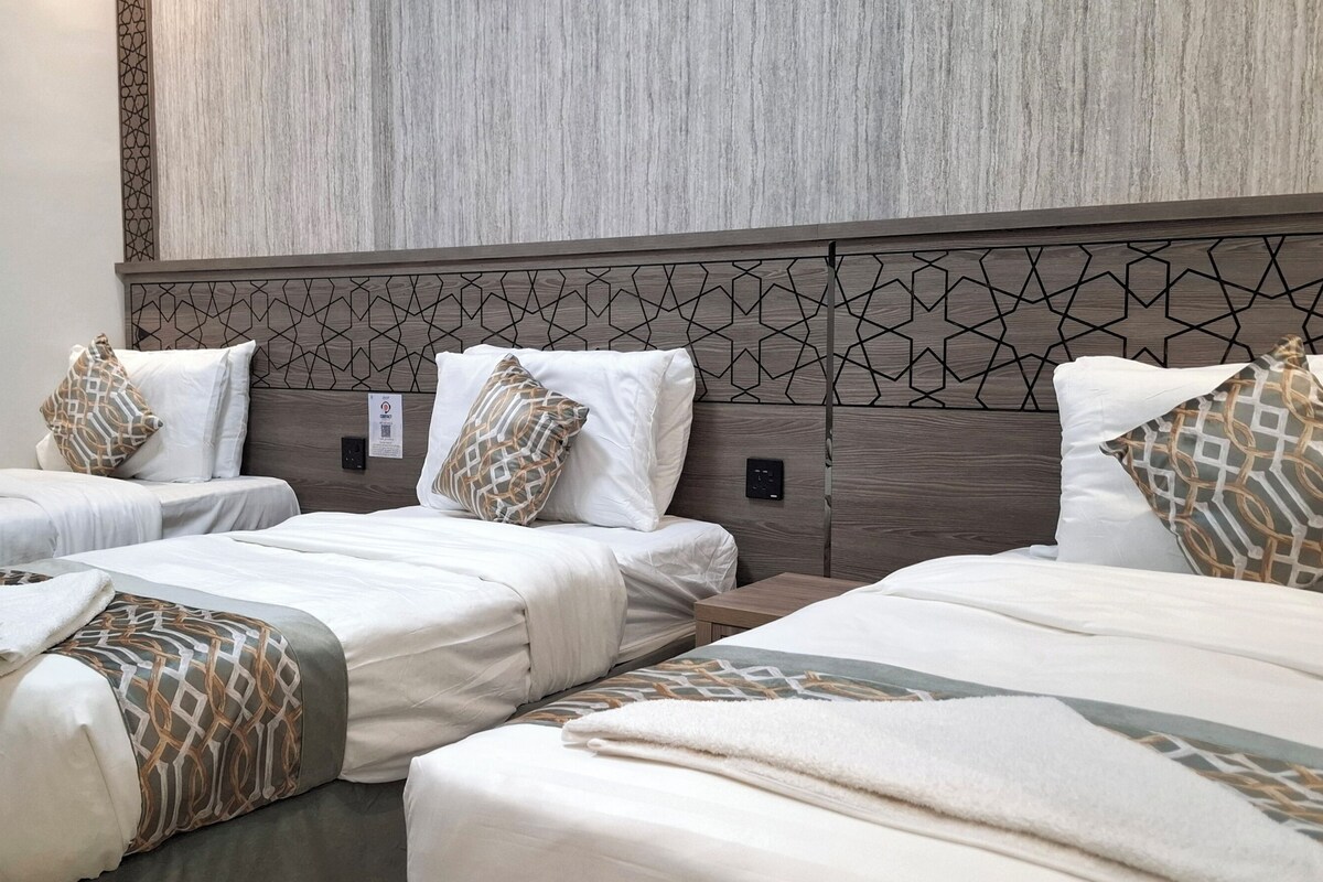 Een hotelkamer met twee eenpersoonsbedden en een groter bed, allemaal met witte lakens en gestreepte kussens.