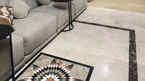 Un salon moderne avec un canapé gris, un tapis à motifs et un téléviseur à écran plat fixé au mur.