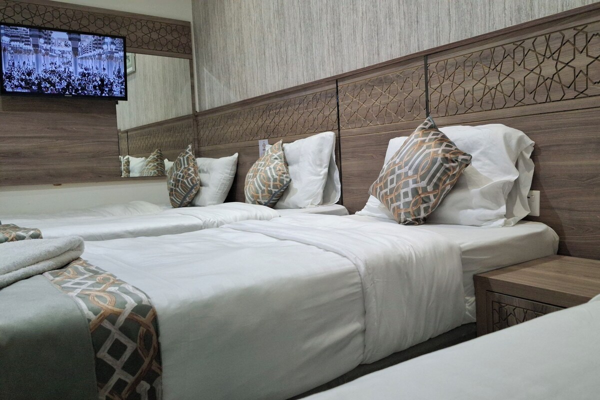 Habitación de hotel con dos camas, un televisor montado en la pared y cabecero de madera con diseños geométricos.