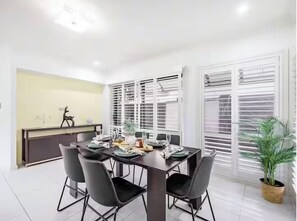 Un coin repas avec une table mise pour quatre personnes, entourée de chaises. Un pot de fleurs se trouve sur le côté droit.