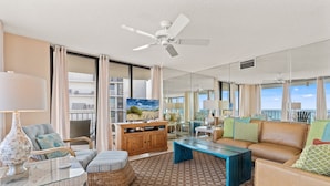 Un salón amplio con ventilador de techo, un ventanal y vista al océano.