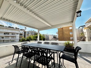 An outdoor patio with a table and chairs, surrounded by a white pergola, overlooking a residential area with buildings and greenery. - PalmbeeCannes 4à6 personnes 70m2+Terrasses à 200m des Plages, 100m du PalmBeach (Cannes)