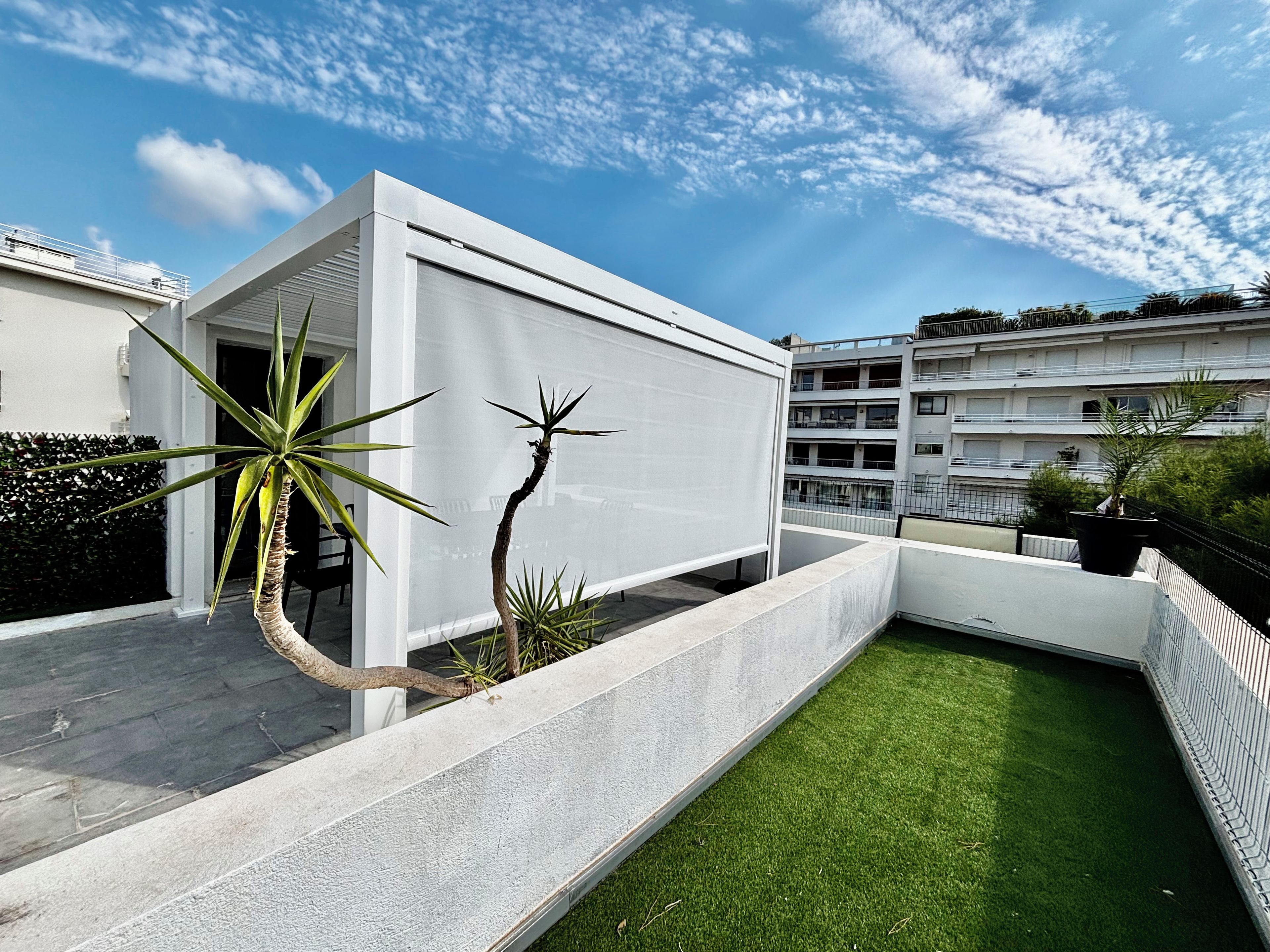A modern building with a flat roof, a balcony, and a small garden area with artificial grass.