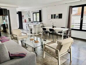 A modern living room with a glass coffee table, a sofa with colorful pillows, and a dining area with a white table and black chairs. - PalmbeeCannes 4à6 personnes 70m2+Terrasses à 200m des Plages, 100m du PalmBeach (Cannes)