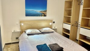 Een slaapkamer met een bed, een houten hoofdbord, een nachtkastje, een wandairconditioner, een groot raam met uitzicht op zee en een kledingkast met meerdere planken.