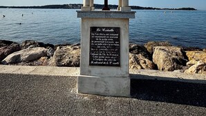 Een monument met een kruis en plaquette aan de kust.