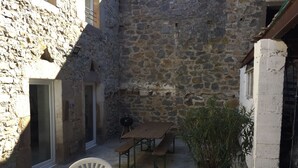 A stone-walled courtyard with a table and chairs, a potted plant, and a grill. - Parenthèse nature au cœur des Gorges du Tarn - Charming house & patio (Rivière-sur-Tarn)
