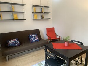 A living room with a brown sofa, two decorative pillows, a red armchair, a small table with a red placemat and a potted plant, and a checkered floor. - Mecenate 7 –  15 Minutes from the City Center (Milano)