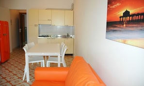 A compact kitchen with a dining area, a red refrigerator, and a sunset painting on the wall. - Comfortable Flat by the Beach (Lignano Sabbiadoro)