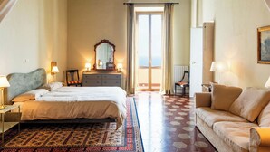 Quarto de hotel com cama, sofá, cômoda, espelho e varanda com vista.