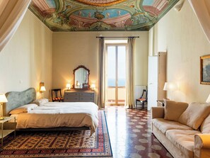 Ein Hotelzimmer mit Bett, Sofa, Schminktisch, Spiegel und einem Balkon mit Blick.
