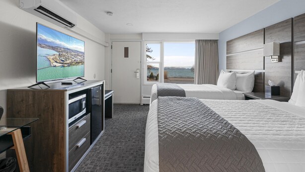 Une chambre d’hôtel avec un lit, un bureau équipé d’un ordinateur, une télévision et une vue sur la mer.