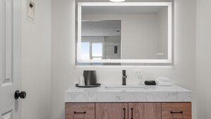Une salle de bain moderne avec un comptoir en marbre blanc, un grand miroir, des armoires en bois et une machine à café.