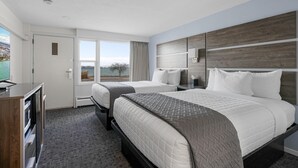 Une chambre d’hôtel avec deux lits, une télévision, un bureau et une fenêtre donnant sur un paysage agréable.